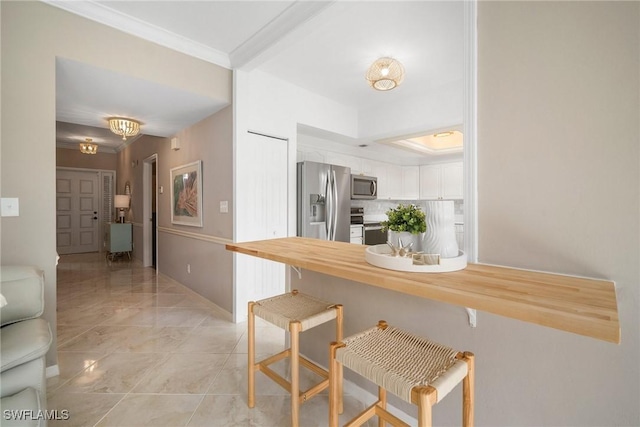 kitchen featuring appliances with stainless steel finishes, a breakfast bar, butcher block counters, white cabinets, and kitchen peninsula