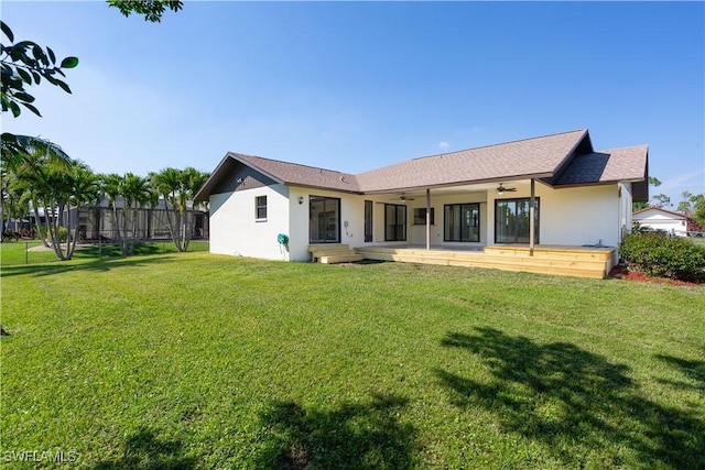 rear view of house featuring a yard, ceiling fan, fence, and stucco siding