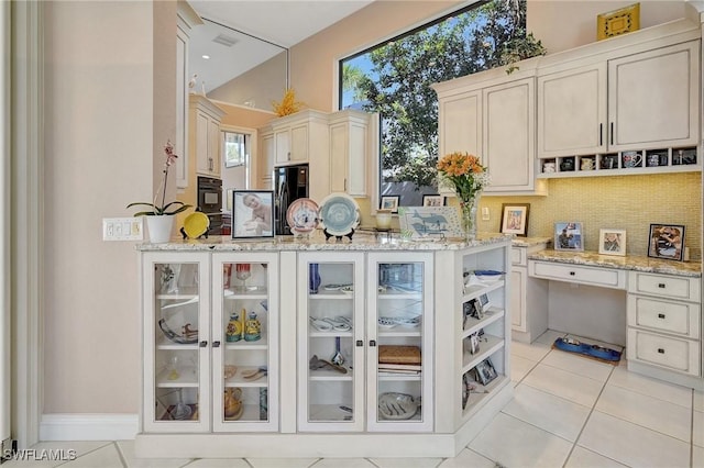 kitchen featuring light stone countertops, light tile patterned floors, black fridge with ice dispenser, and backsplash