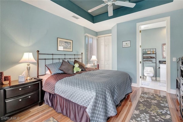 bedroom with ensuite bath, light hardwood / wood-style flooring, ceiling fan, a raised ceiling, and a closet