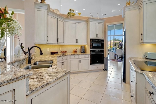 kitchen with sink, decorative backsplash, light tile patterned floors, light stone counters, and black appliances