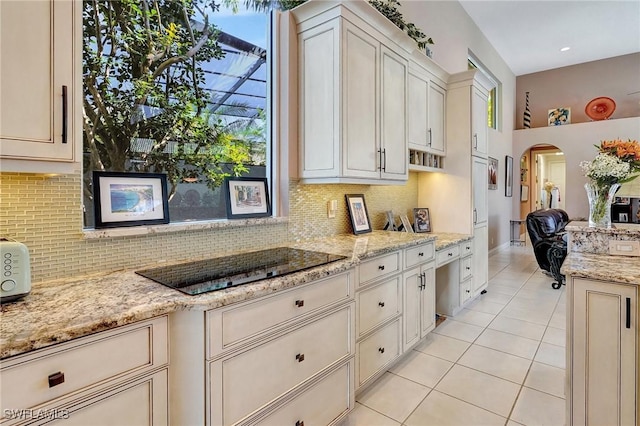 kitchen with tasteful backsplash, black electric stovetop, light tile patterned floors, and light stone counters