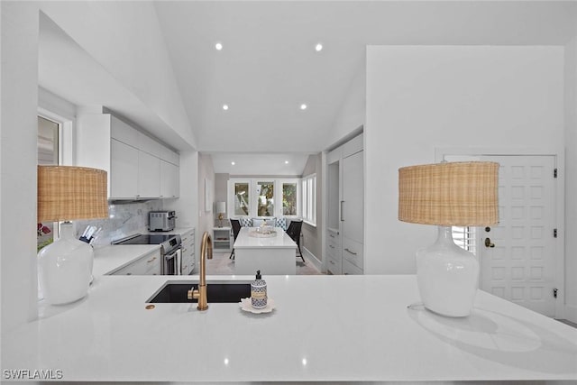 kitchen featuring sink, white cabinets, decorative backsplash, stainless steel range with electric stovetop, and kitchen peninsula