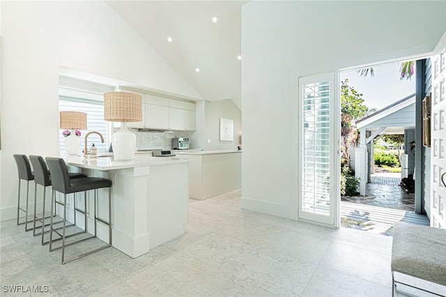 kitchen with sink, a breakfast bar area, white cabinets, decorative backsplash, and kitchen peninsula