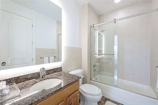 full bathroom with tile walls, vanity, bath / shower combo with glass door, and toilet