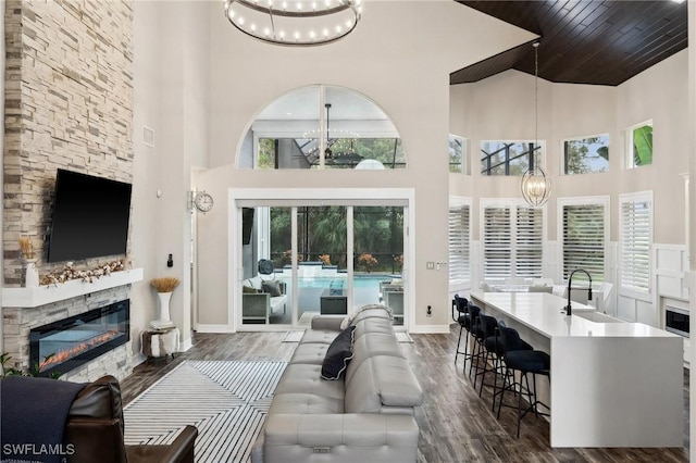 living room featuring dark wood-type flooring, a stone fireplace, sink, and a notable chandelier