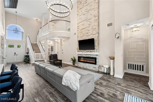 living room featuring an inviting chandelier, a fireplace, dark hardwood / wood-style flooring, and a towering ceiling