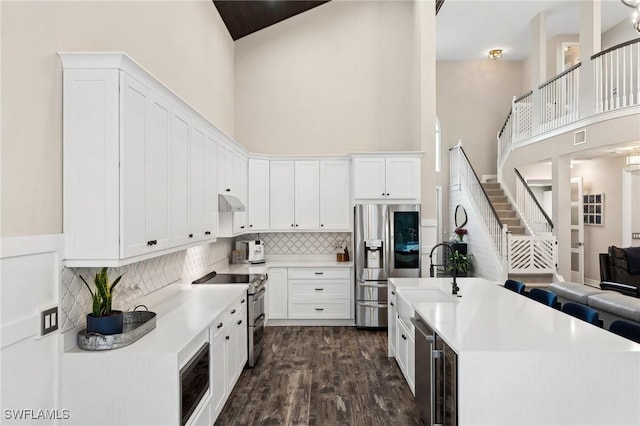 kitchen with stainless steel appliances, sink, white cabinets, and a towering ceiling