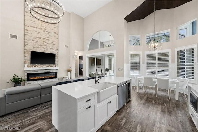 kitchen with an island with sink, sink, white cabinets, stainless steel dishwasher, and a notable chandelier