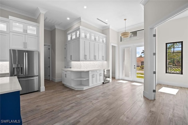 kitchen with tasteful backsplash, hanging light fixtures, stainless steel fridge, and white cabinets