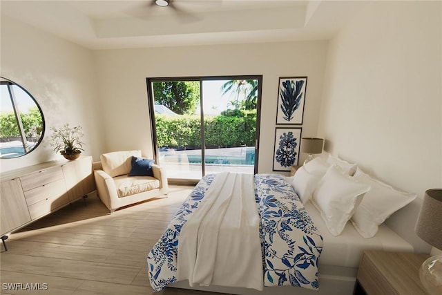 bedroom with ceiling fan, access to exterior, light wood-type flooring, and a tray ceiling