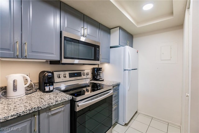 kitchen featuring light stone counters, stainless steel appliances, a raised ceiling, and light tile patterned floors