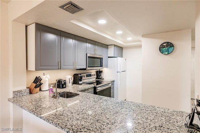 kitchen featuring sink, gray cabinets, stainless steel appliances, light stone counters, and a tray ceiling