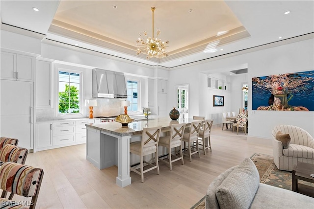 565 Anchor Rode Dr, Naples, FL 34103 - kitchen featuring wall chimney range hood, a breakfast bar, a tray ceiling, and a notable chandelier