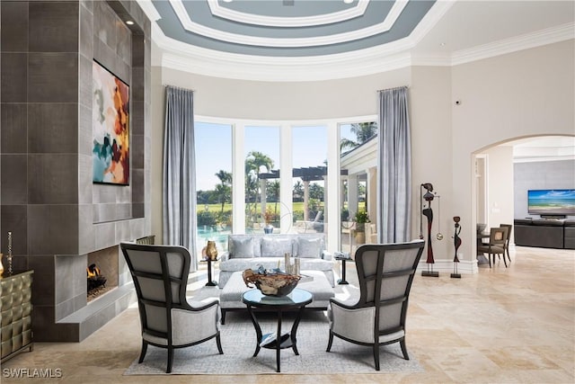 living area with a high ceiling, ornamental molding, a large fireplace, and a tray ceiling