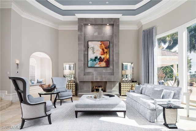 living room featuring arched walkways, a high ceiling, a large fireplace, and ornamental molding