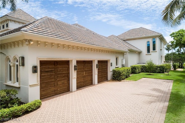 exterior space featuring a garage, stucco siding, a tiled roof, and decorative driveway