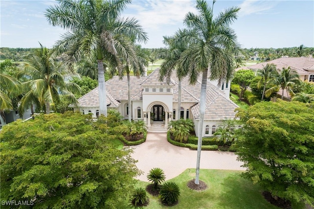 mediterranean / spanish house featuring a tile roof, a front lawn, and stucco siding