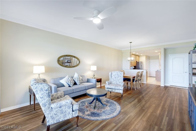 living room with dark wood-type flooring, crown molding, and ceiling fan with notable chandelier