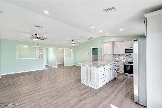 kitchen with appliances with stainless steel finishes, lofted ceiling, white cabinets, a center island, and light stone counters