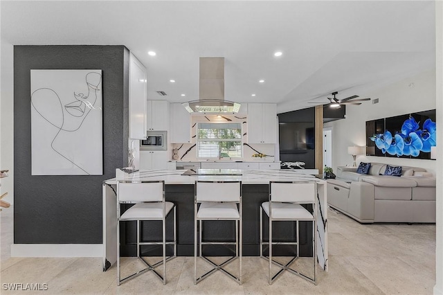 kitchen with stainless steel microwave, island range hood, a breakfast bar area, white cabinets, and kitchen peninsula