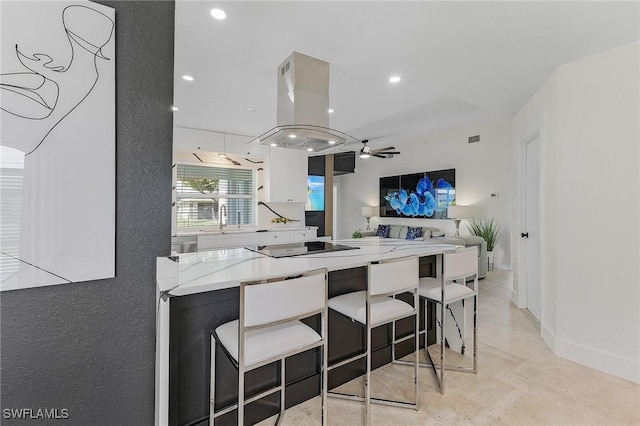 kitchen featuring sink, a breakfast bar area, ceiling fan, light stone counters, and island range hood