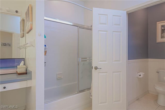 full bathroom featuring a wainscoted wall, combined bath / shower with glass door, toilet, and tile patterned floors