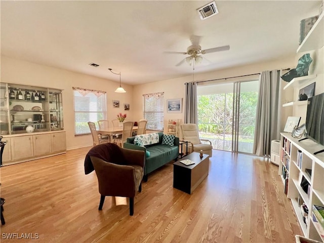 living room with a ceiling fan, visible vents, plenty of natural light, and wood finished floors