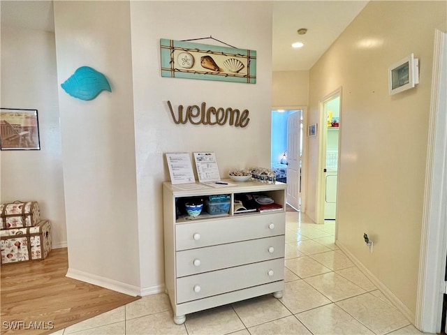 corridor featuring washer / clothes dryer, light tile patterned flooring, and baseboards