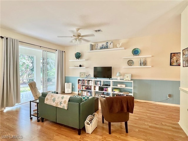 living area with wainscoting, wood finished floors, visible vents, and a ceiling fan