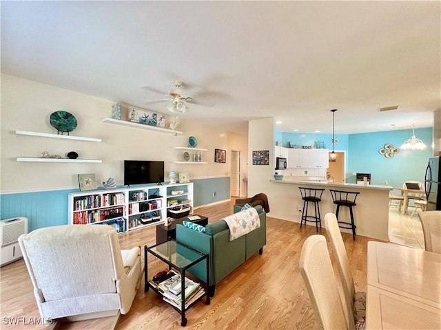 living area with a wainscoted wall, visible vents, ceiling fan with notable chandelier, and light wood-style flooring