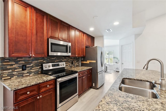 kitchen with tasteful backsplash, sink, light stone counters, light hardwood / wood-style floors, and stainless steel appliances