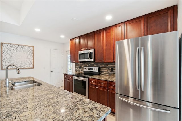 kitchen with light stone counters, stainless steel appliances, sink, and decorative backsplash