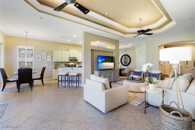 tiled living room featuring crown molding, a tray ceiling, and ceiling fan