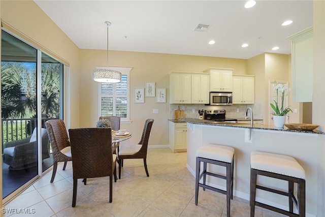 kitchen with appliances with stainless steel finishes, pendant lighting, tasteful backsplash, dark stone countertops, and kitchen peninsula