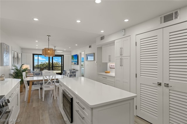 kitchen with decorative light fixtures, built in microwave, white cabinetry, a center island, and light wood-type flooring