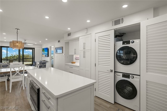 kitchen featuring white cabinetry, stacked washer and clothes dryer, a kitchen island, built in microwave, and decorative light fixtures