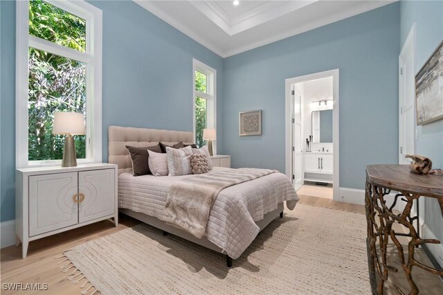 bedroom with ensuite bath, ornamental molding, a raised ceiling, and light hardwood / wood-style floors