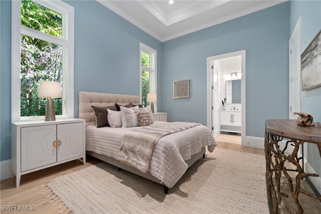 bedroom with light wood finished floors, baseboards, ensuite bath, a tray ceiling, and crown molding