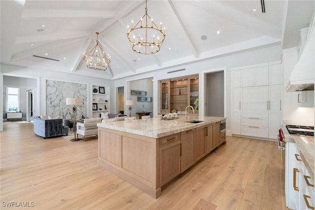 kitchen with light brown cabinetry, sink, pendant lighting, a large island, and light stone countertops