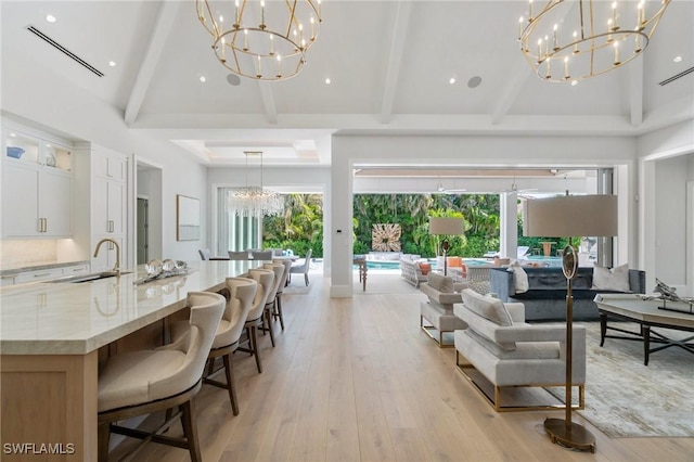 living room featuring light wood-type flooring, high vaulted ceiling, sink, and a notable chandelier