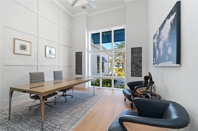 office featuring crown molding, wood finished floors, a towering ceiling, and a decorative wall