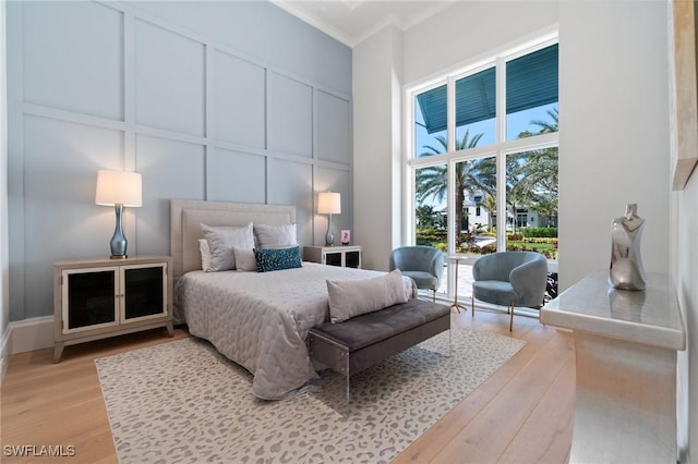 bedroom with light wood-style floors, ornamental molding, and a decorative wall