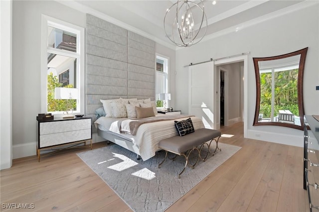 bedroom with a barn door, a notable chandelier, light wood-type flooring, and a tray ceiling