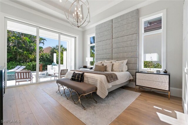 bedroom with an inviting chandelier, access to outside, light hardwood / wood-style floors, and a tray ceiling