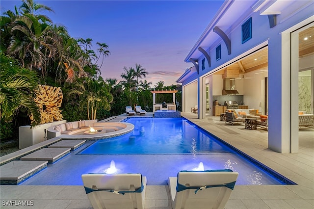 pool at dusk with a patio, an in ground hot tub, exterior kitchen, a fenced in pool, and an outdoor living space with a fire pit