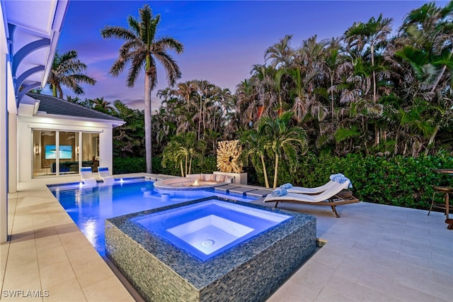 pool at dusk featuring an outdoor pool, a patio, and an in ground hot tub