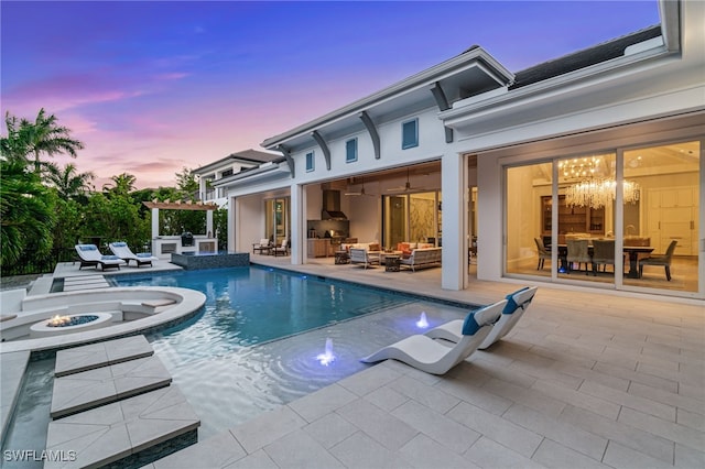 pool at dusk featuring a patio, an outdoor kitchen, an outdoor living space with a fire pit, and a pool with connected hot tub