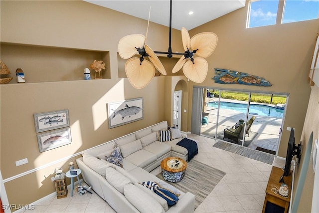 living room with a towering ceiling, ceiling fan, and light tile patterned flooring