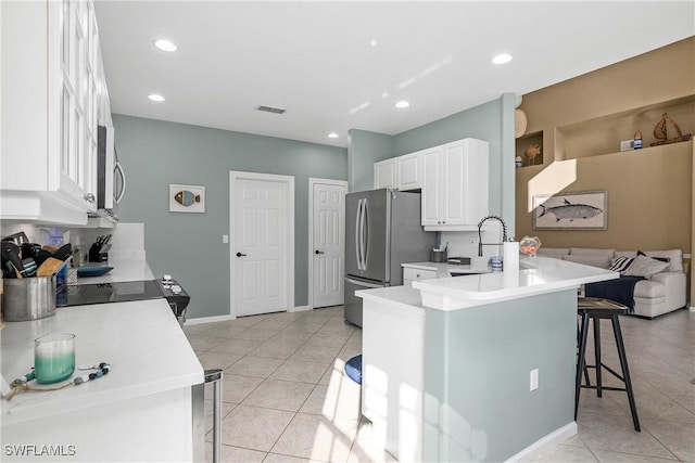 kitchen featuring a breakfast bar, stainless steel refrigerator, sink, white cabinets, and kitchen peninsula